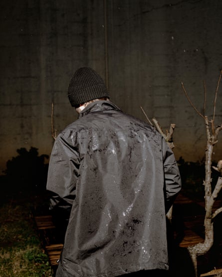A boy wearing a coat in the rain facing away in the dark