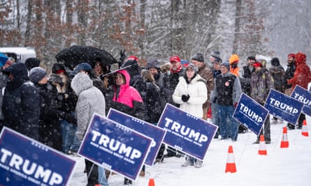 a line of people in winter coats in the snow with Trump signs around them