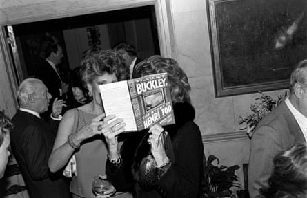 two women hold a book by William F Buckley, which covers their faces, at a party