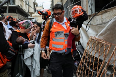 Adults in high visibility clothing carry children away from an impact site