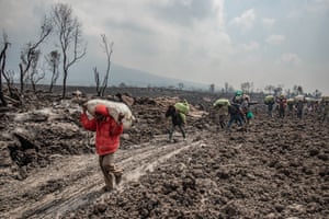 Residents carry their belongings on their backs as they cross a cooling lava-covered field in Buhene, north of Goma
