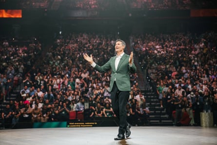 a man in a suit walks in stage in an arena full of people