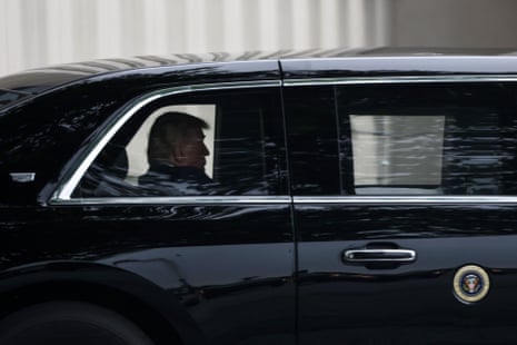 A man sits in back of a black limo with a presidential seal on the side of the door