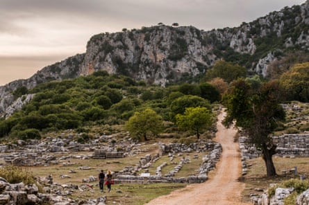 Ruins around a track under olive trees and cliffs