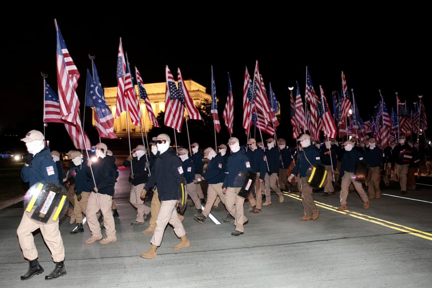 Group of men in blue shirts, khaki pants and balaclavas holding American flags