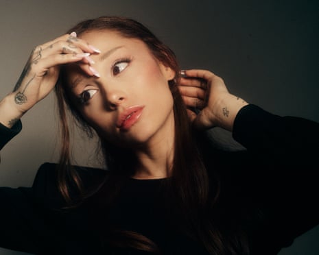 Ariana Grande holds her hands around her head, dressed in gothic black clothing
