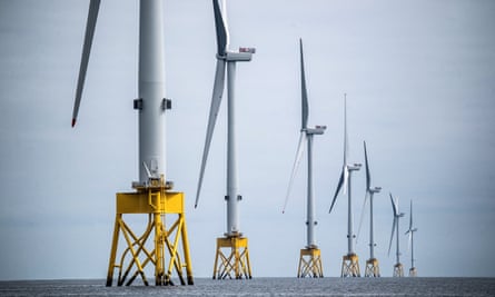 Seven turbines in a line at the Seagreen offshore windfarm, off the coast of Montrose, Angus, in the North Sea. Their blades and tall masts are white and they are mounted on yellow bases which rise out of the water. 