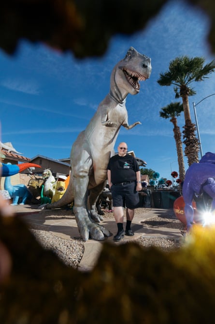 A man stands beneath a large dinosaur in the driveway
