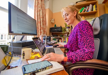 Linda Geddes sitting at a desk in front of a computer, a laptop and looking at her phone