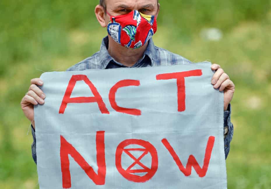 Man in a face mask holds banner saying Act Now