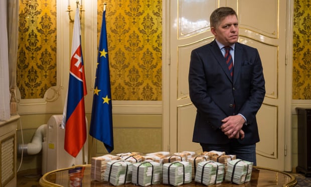 Robert Fico stands behind bundles of euros in Bratislava.