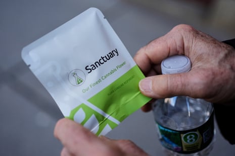 A close-up of a man holding green and white pouch containing cannabis.