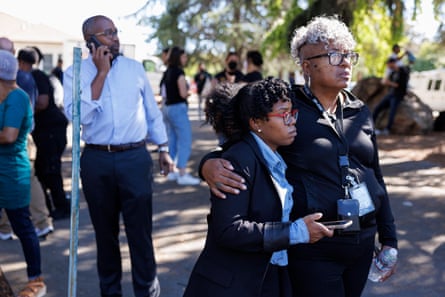 A woman stands with her arm around another woman as people mill about an open space.