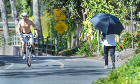 With temperatures in the 80s, a shirtless cyclist rides past a woman shading herself with an umbrella as they make their way along the Hicks Canyon Trail in Irvine, California, on Tuesday.