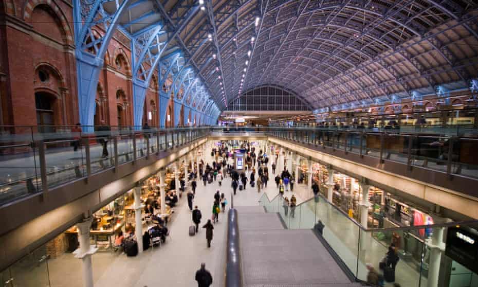 Picture of London St Pancras with people walking along the sunken concourse and its famous arched roof illuminated in purple and blue