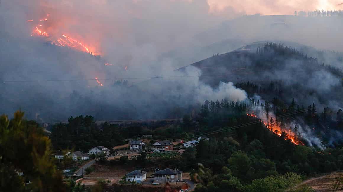 A wildfire and smoke sweep down a mountain towards a village