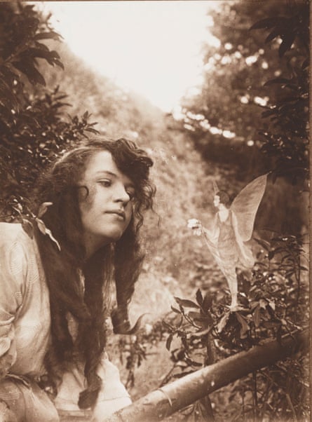 A sepia image of a young girl, tress all around, looking at what appears to be a fairy