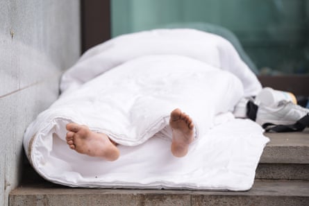 A homeless person covered in a white duvet on steps
