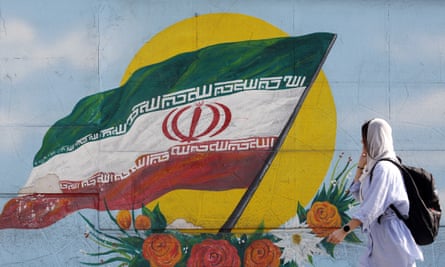 A woman walks past a wall with the Iranian national flag painted on it in Tehran, Iran