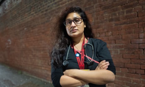 Pushpo Hossain, wearing an ID lanyard and a stethoscope, standing outside with her arms folded in front of a red-brick wall