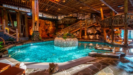 An illuminated indoor pool surrounded by wooden structures and natural stones