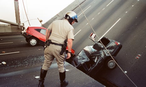 In a 17 October 1989 photo, a California highway patrol officer checks the damage to cars that fell when the upper deck of the Bay Bridge collapsed onto the lower deck after the Loma Prieta earthquake in San Francisco. 