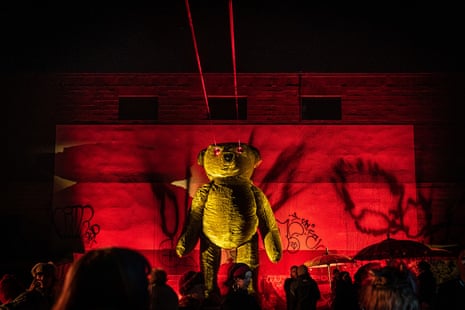A huge teddy bear on stage backlit with a red light and laser beams coming from its eyes