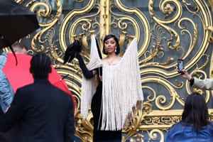 Cardi B wearing a black dress with huge beaded neckpiece that envelops the upper part of her body. She is also holding a live crow