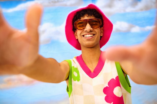 Young man blocking camera with hand enjoying colourful fashion