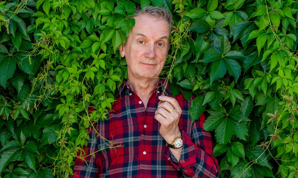 Frank Skinner, comedian, actor, presenter and writer standing in a hedge of virginia creeper wearing a check shirt