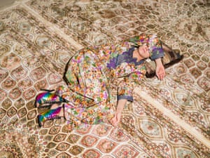 Woman in patterned clothes asleep on a similarly patterned carpet.