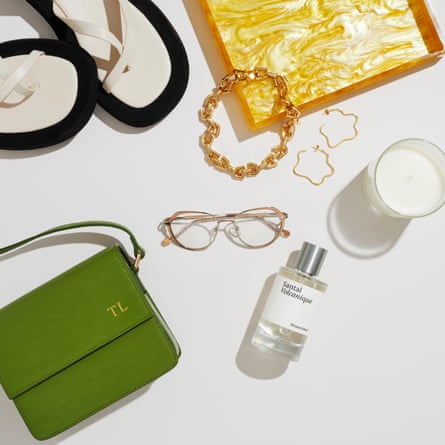 Eyeglasses in the centre. Sandals, gold bracelet and earrings, candle, perfume and green handbag scattered around it