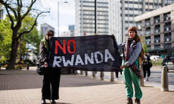 Two people holding up a black banner with no Rwanda written on top in red and white