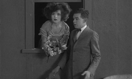 Clara Bow holding flowers leaning out of window with James Turfler in The Pill Pounder.