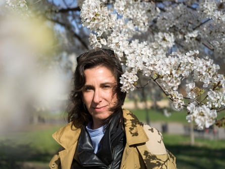A woman in a trenchcoat stands with blossom tree branches around her head.
