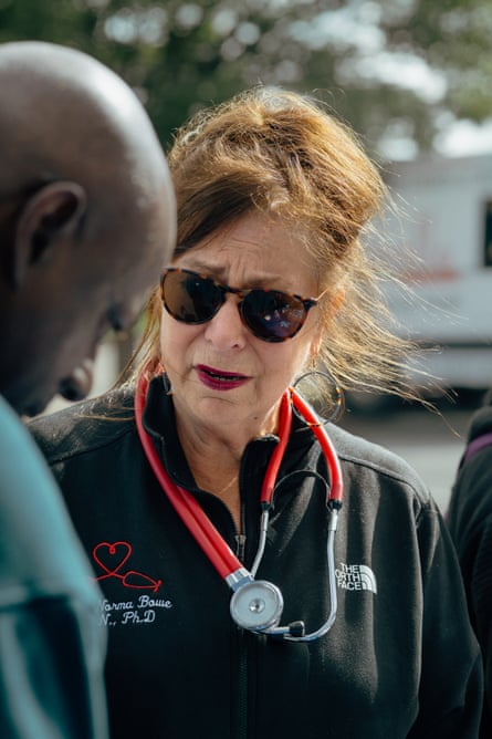 A woman wearing sunglasses and a stethoscope speaks with a man