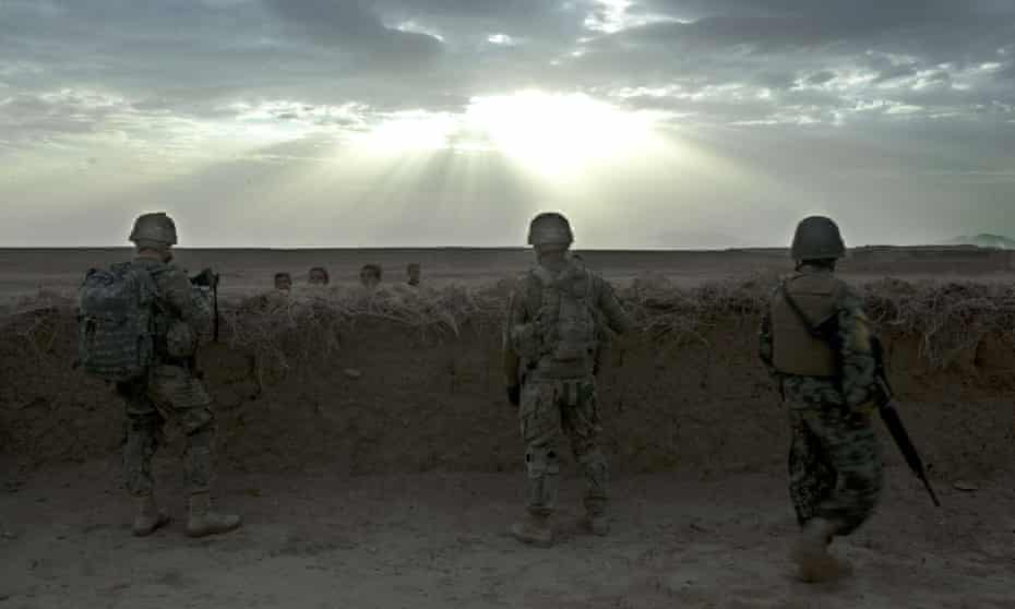 Two US soldiers with an Afghan colleague (right) secure a position behind a mud wall in Daman district, Kandahar, Afghanistan