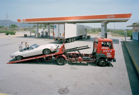 A sports car being loaded onto a tow truck in front of a petrol station