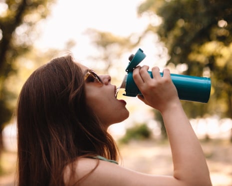 Young woman drinking water from reusable bottle in summer park