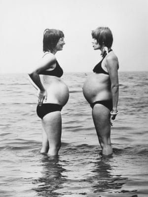 Two pregnant women in bikinis talk in the sea at the beach