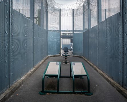 A small exercise yard surrounded by high metal fences with barbed wire at the top.