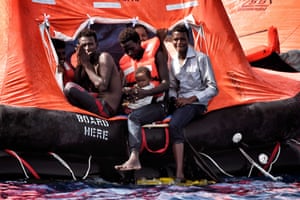 Migrants wait to be rescued with a baby in their arms