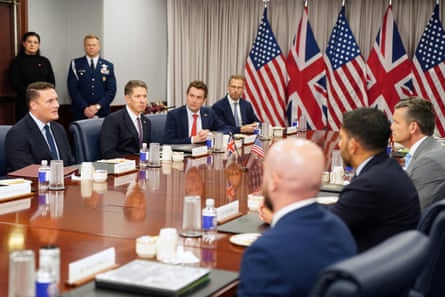 Streeting and Hegseth sit on opposite sides of a long table with colleagues alongside each of them and flags at the far end of the room