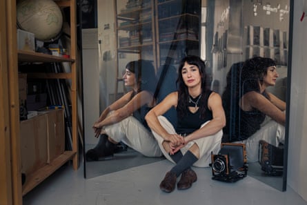 Artist Hoda Afshar sits cross-legged between mirrors in her studio, beside a vintage camera