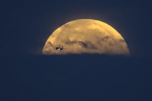 An airplane flies past as the full-moon sets over Santa Monica Beach in Santa Monica, California, US
