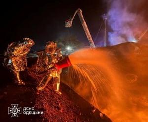 A night shot of two firefighters in metallic heat-resistant suits spraying foam on to a fire