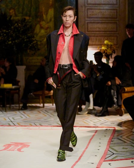 A model wearing a relaxed suit, with the pink shirt unbuttoned and the trouser belt undone.