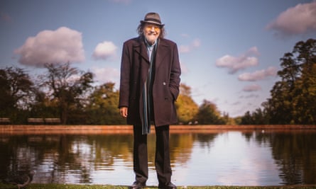Fay pictured this year standing in front of a lake and wearing a knee-length overcoat and a trilby