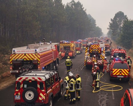 Firefighters and their vehicles stretch back as far as the eye can see on a road with woodland on either side