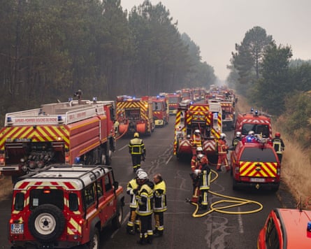 Firefighters and their vehicles stretch back as far as the eye can see on a road with woodland on either side